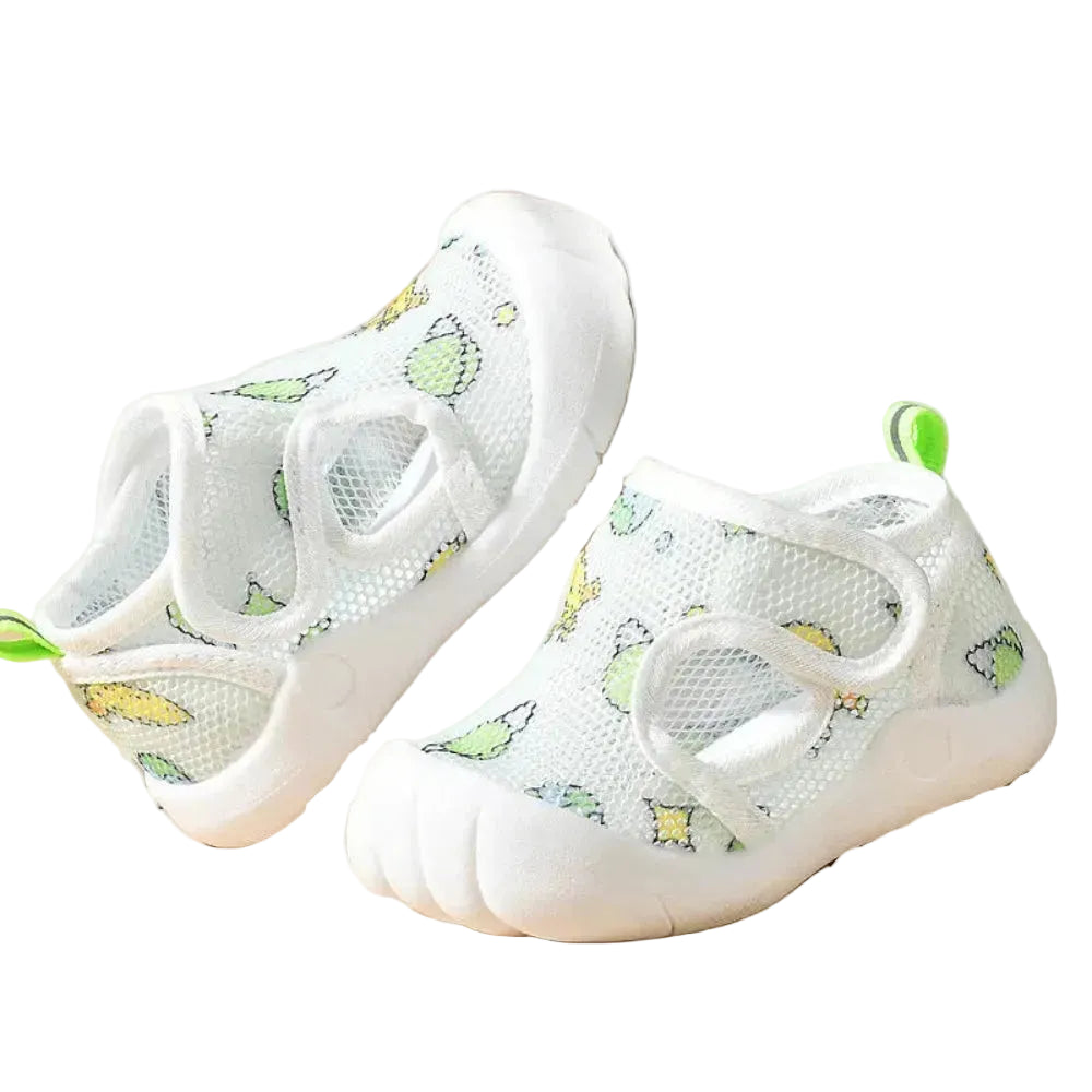 White children's sandals with green accents on a beige surface