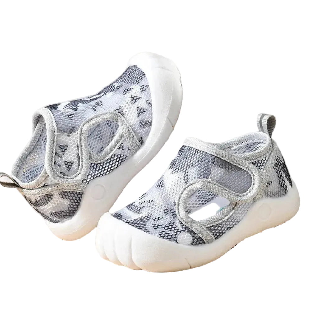 Pair of gray and white mesh shoes on a beige surface with a white box in the background.